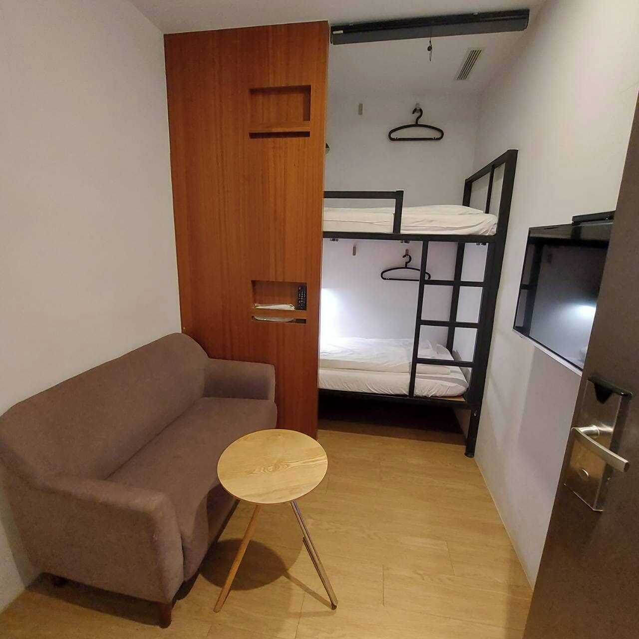 A small room with a sofa, a round table, a bunk bed, and a TV.