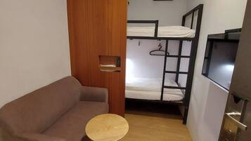 A small room with a sofa, a round table, a bunk bed, and a TV.