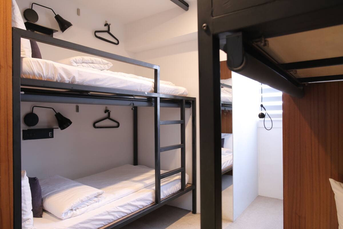 Habitación con literas, una escalera, una lámpara colgante y un perchero.