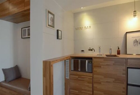 Una cocina moderna con encimera de madera, microondas integrado y un lavamanos. Un cartel en la pared dice "MINI BAR".