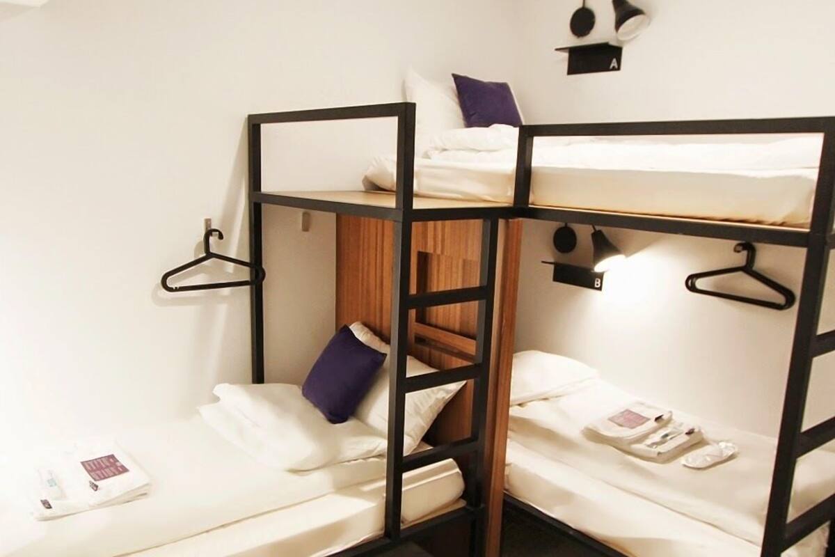 Dormitorio con literas, escalera de madera, ropa de cama blanca y una mesita con un libro y un control remoto.
