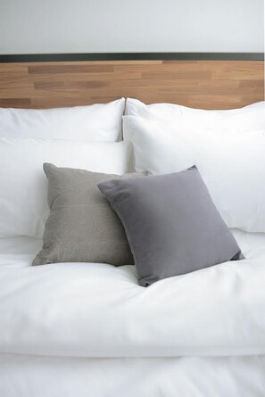 A bed with white bedding and two pillows, one grey and one dark grey.