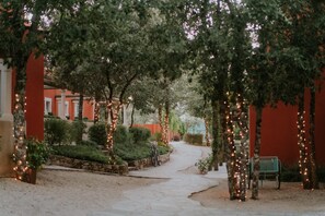 A pathway lined with trees and string lights, leading to a building with red walls and a bench. - Luz Charming Houses (Ourem)