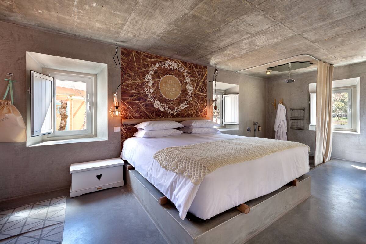 A modern bedroom with a large bed, a decorative wall, and a view of the outdoors.