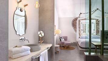 A modern bathroom with a large mirror, a sink, and a vanity. There is a bed visible through a glass partition.