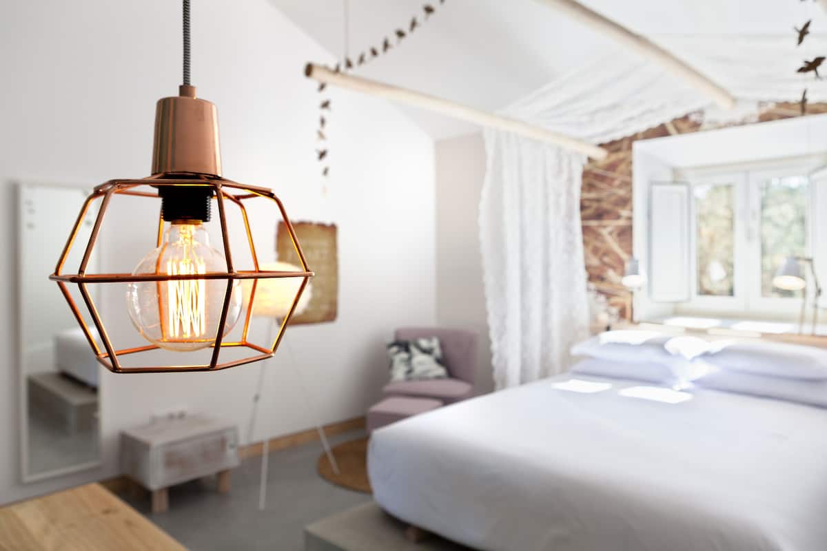 A modern bedroom with a large bed, a bedside table, and a hanging light fixture.