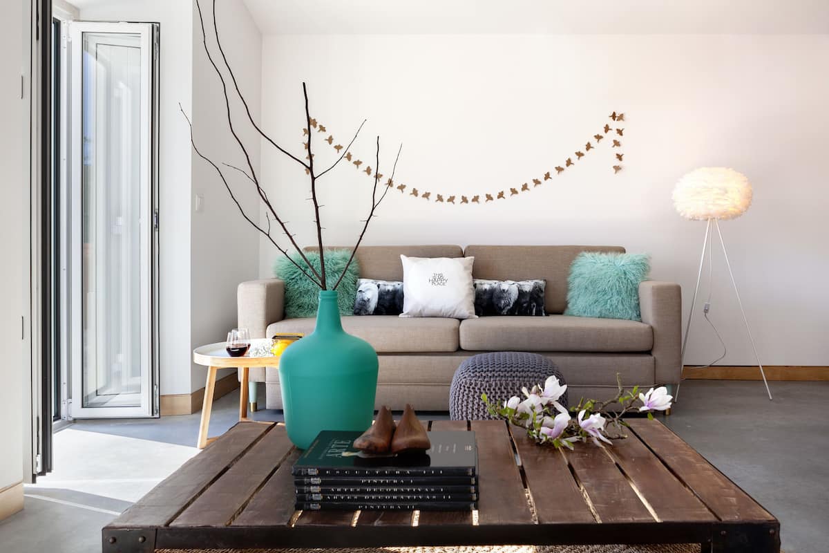 A modern living room with a sofa, a coffee table with books and a vase, and a decorative string of leaves on the wall.