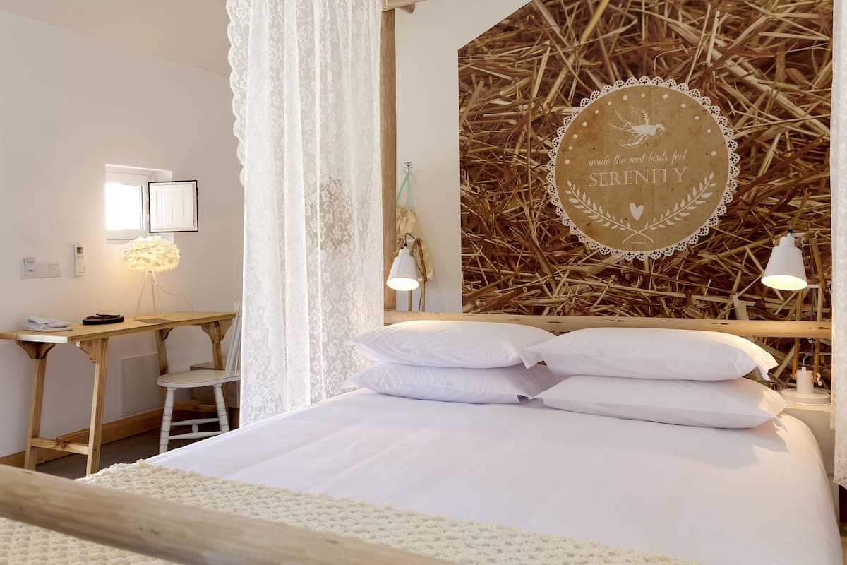 A bedroom with a wooden desk, a chair, a bed with white bedding, and a wall with a circular design featuring a dove and the words "Serenity".