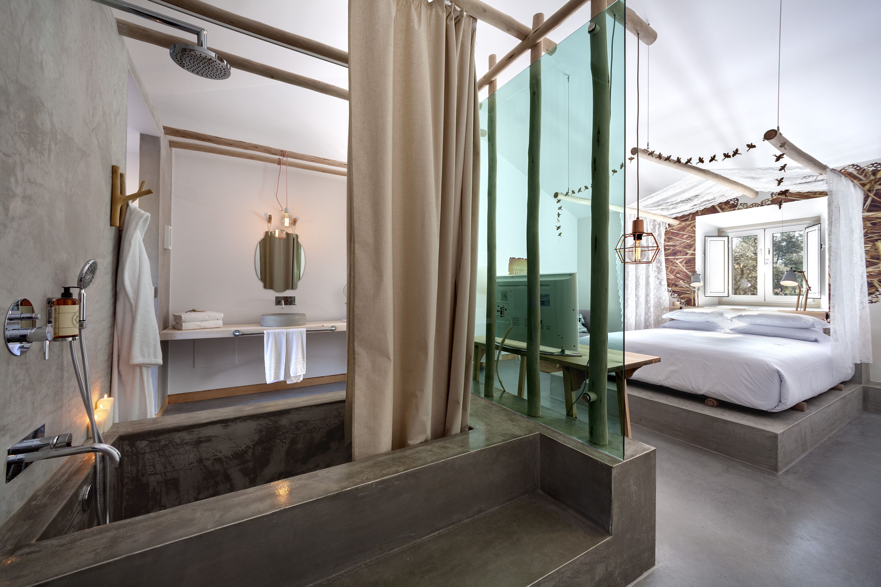 Un baño moderno con ducha, espejo y tocador. En la habitación contigua, hay una cama con ropa blanca.