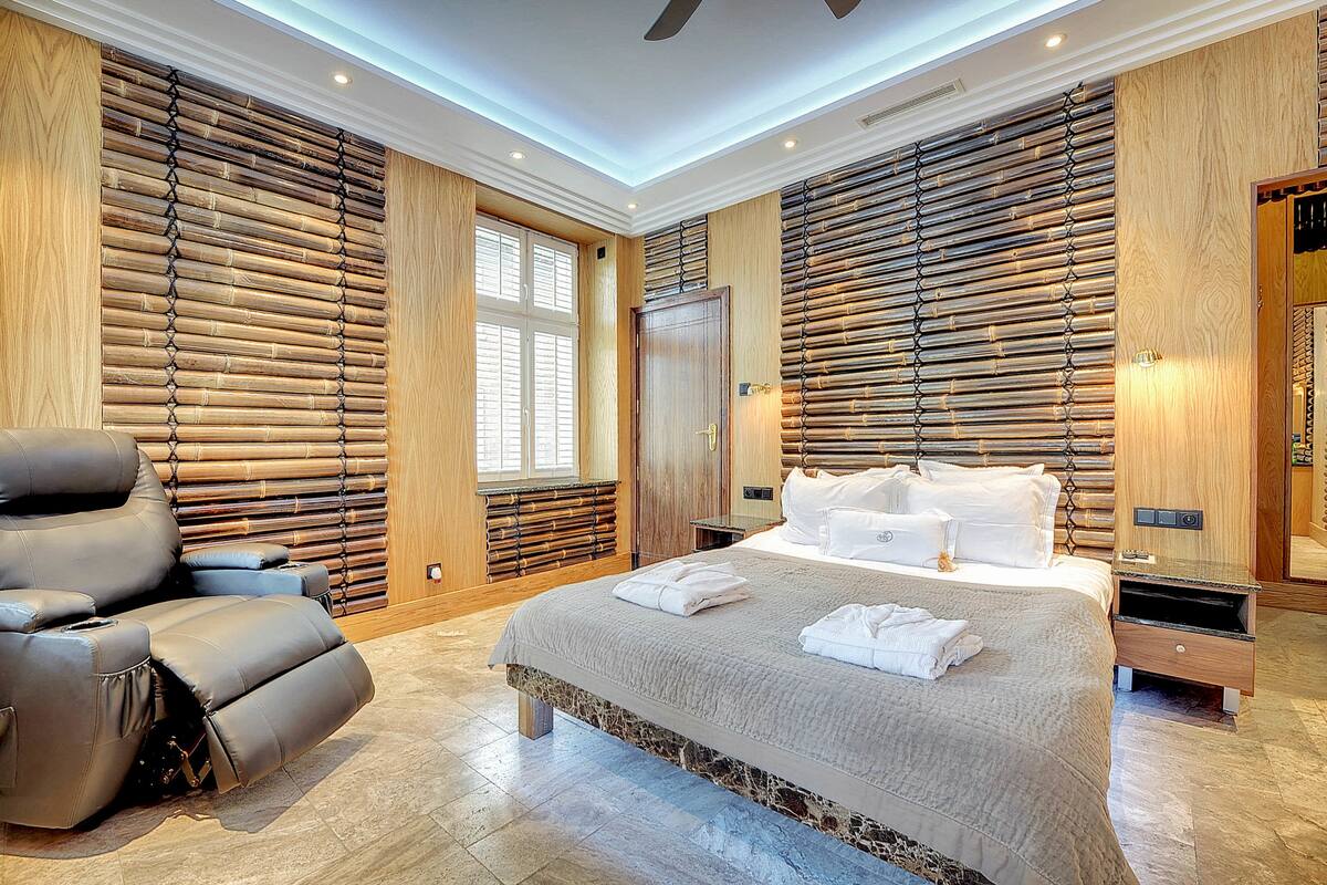 Ein modernes Schlafzimmer mit einem großen Bett, einem Liegesessel und Holzvertäfelung an den Wänden.
