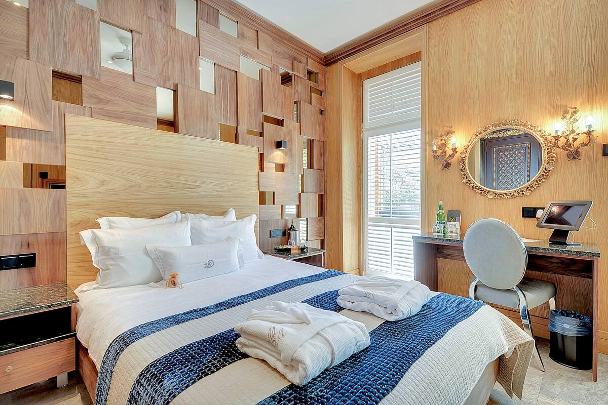 Ein Hotelzimmer mit Holz-Kopfteil, einem Bett mit weißer Bettwäsche, einem Schreibtisch mit Computer und einem Stuhl.