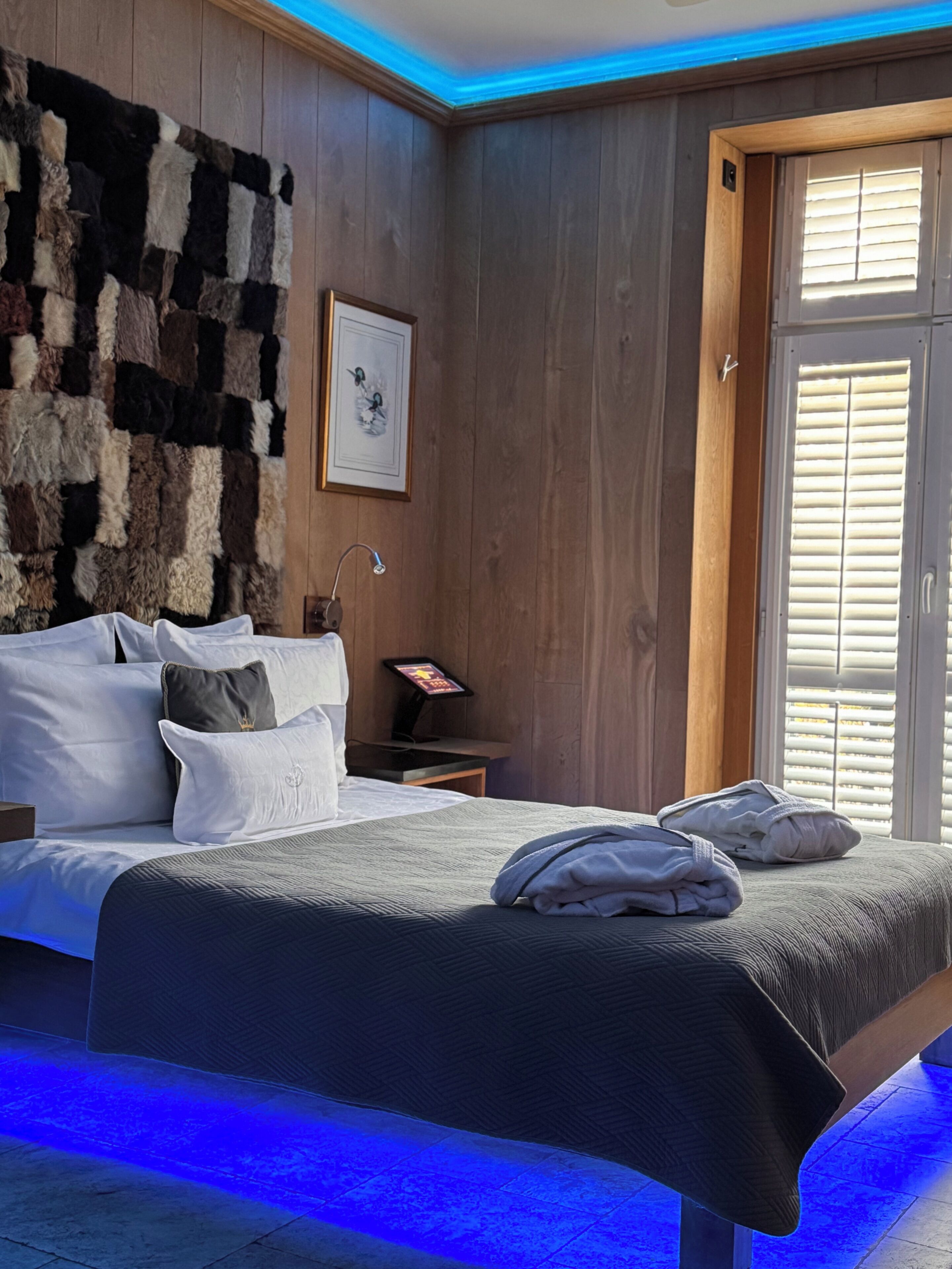 A bedroom with a bed, pillows, a nightstand, a wall-mounted picture, and a window with blinds.