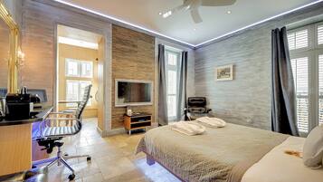 Una habitación de hotel con una cama, un escritorio con computadora, una silla, un televisor y un ventilador de techo.