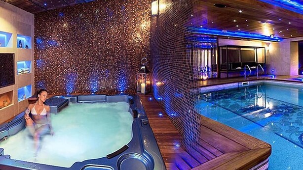 Un jacuzzi con muelle de madera, una piscina y una pared decorativa con luces.