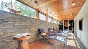 Una habitación iluminada por el sol, con techo de madera, pared de ladrillo y terraza de madera con tumbonas.