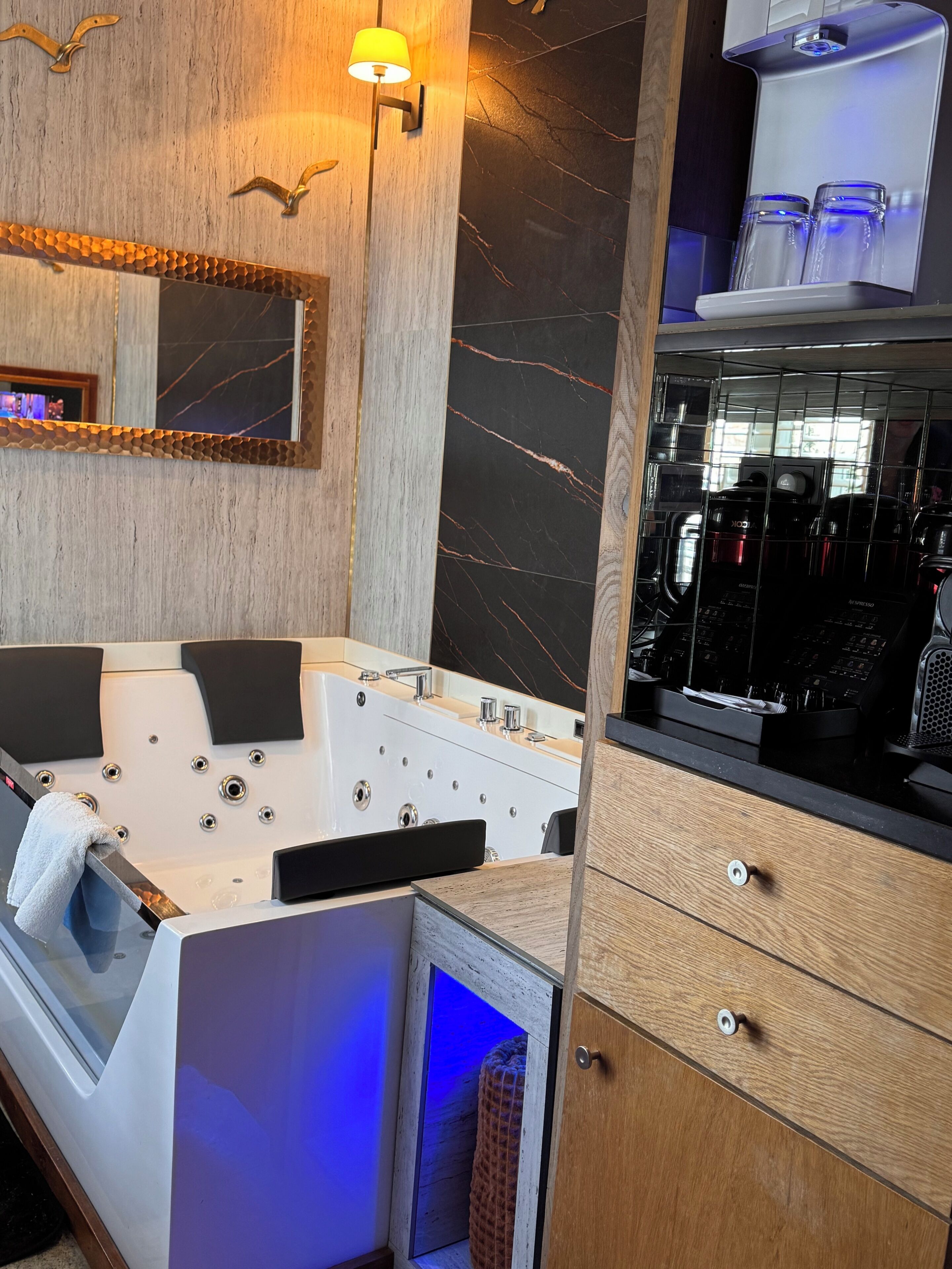 A modern bathroom with a large bathtub, a mirror, a towel rack, and a coffee machine.