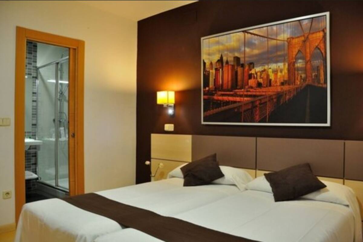 A hotel room with a bed, a large framed picture of a bridge, and a glass door leading to a balcony.