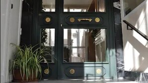 Une porte noire ornée de motifs dorés, avec un pot de plante placé à côté.