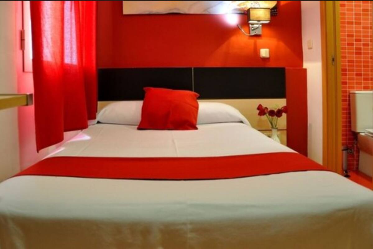 A bed with a red bedspread and pillows, a black headboard, and a wall-mounted light fixture.