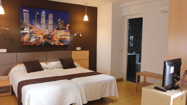 Une chambre d’hôtel avec un grand lit, une télévision, un bureau et un tableau représentant un paysage urbain accroché au mur.