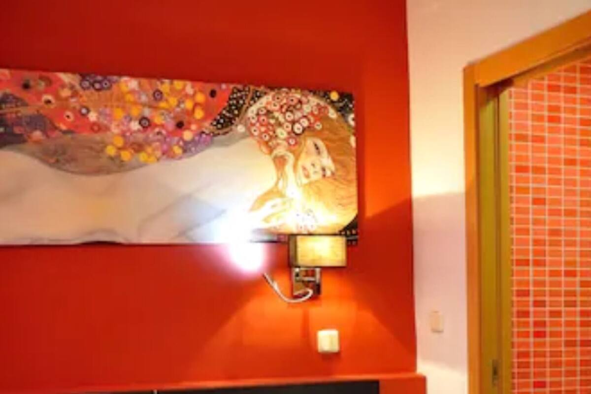 A hotel room with a bed, a wall-mounted light, and a painting above the bed.