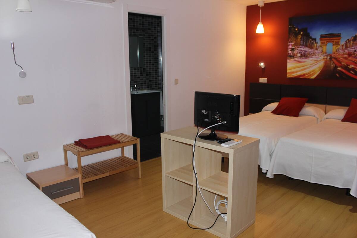 A hotel room with a bed, a TV, a small wooden table, and a painting on the wall.