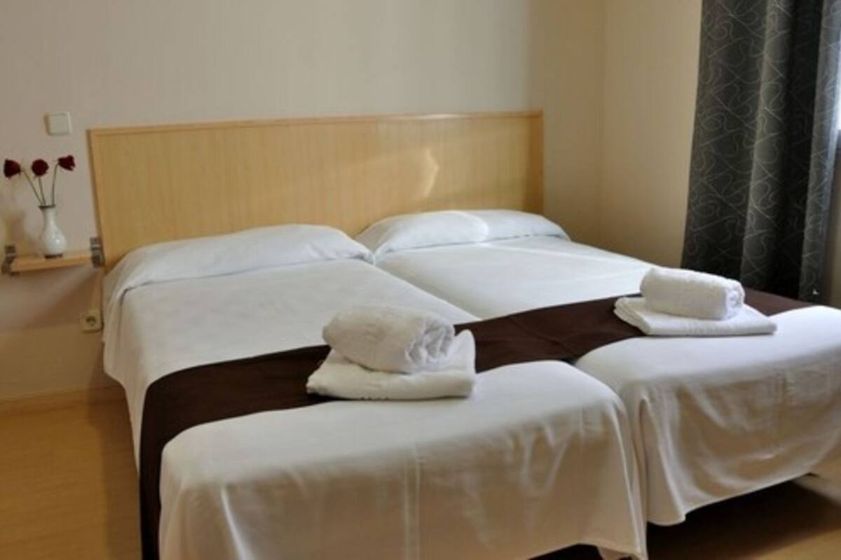 A double bed with white linens and two towels on the bed.