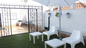 Une terrasse extérieure avec des chaises et des tables en plastique blanc, un parasol blanc et un portail en métal.