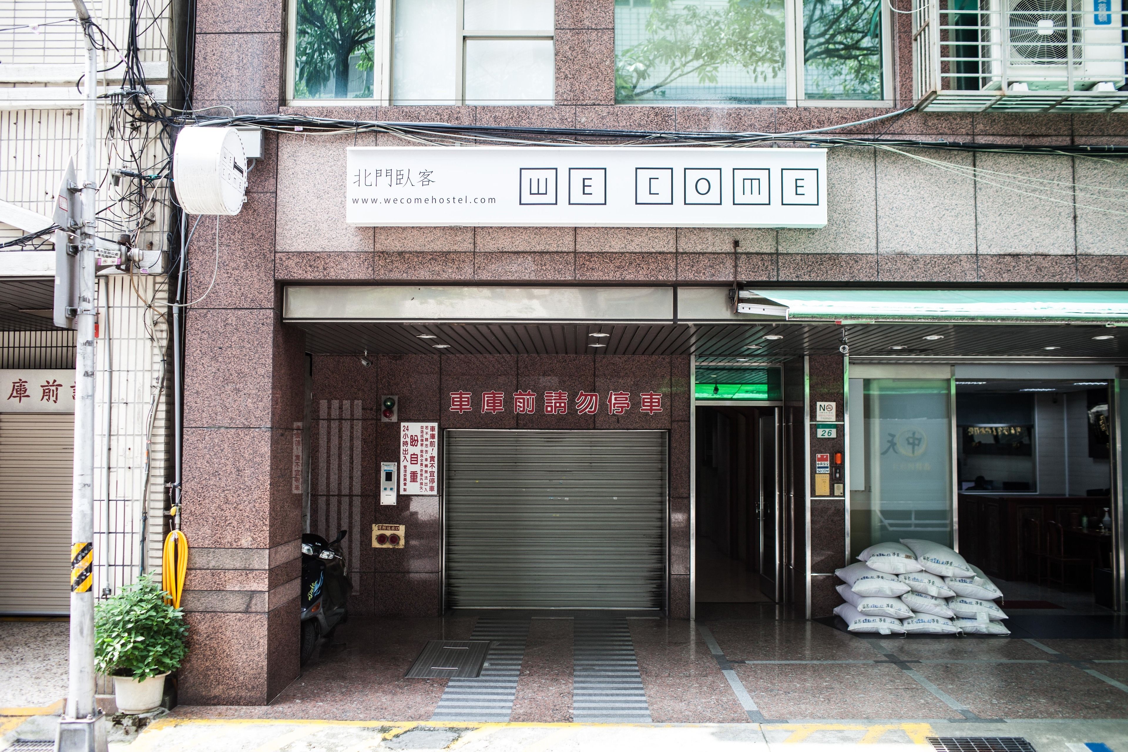 A building entrance with a "WELCOME" sign, a closed garage door, and a sign indicating no parking in front of the garage.
