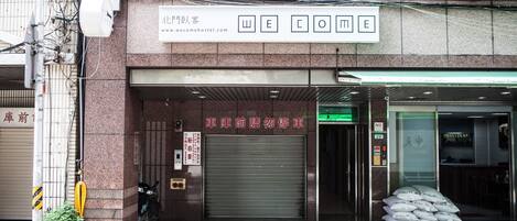 A building entrance with a "WELCOME" sign, a closed garage door, and a sign indicating no parking in front of the garage.
