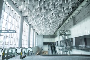 A modern interior with a ceiling of hanging white structures, glass railings, and an escalator. - We Come Hostel (Taipei)