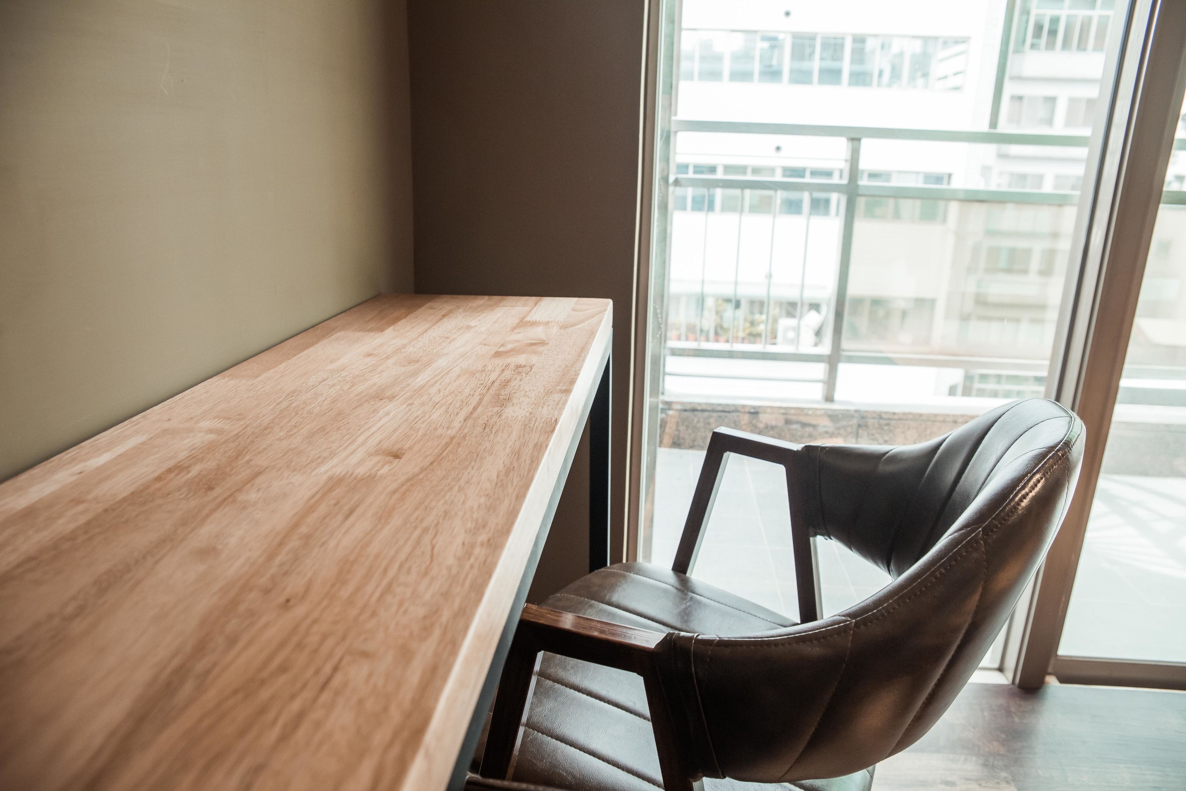 A corner of a room with a wooden desk and a black leather chair.