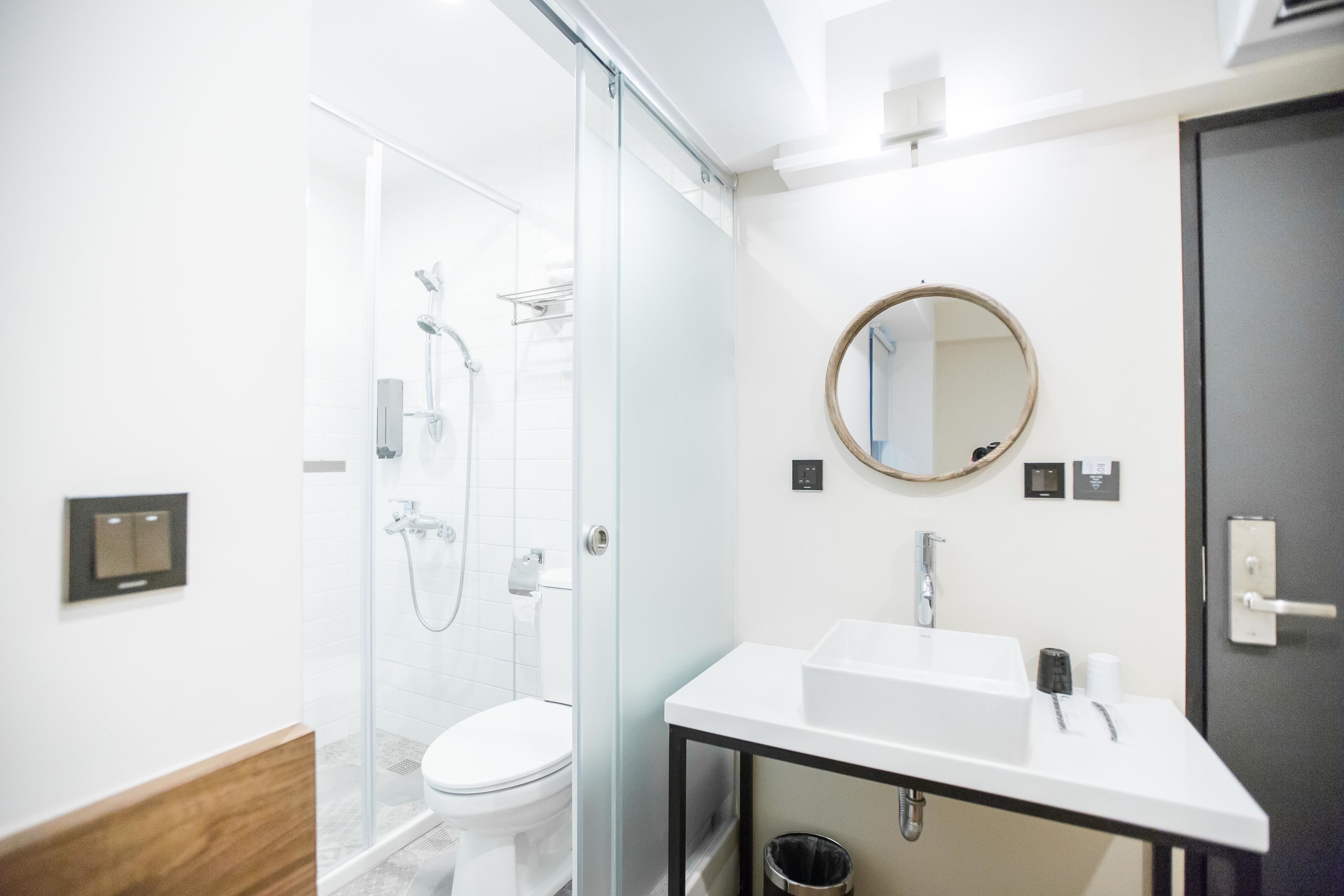 A modern bathroom with a glass shower enclosure, a white toilet, a white sink with a mirror, and a wooden vanity.