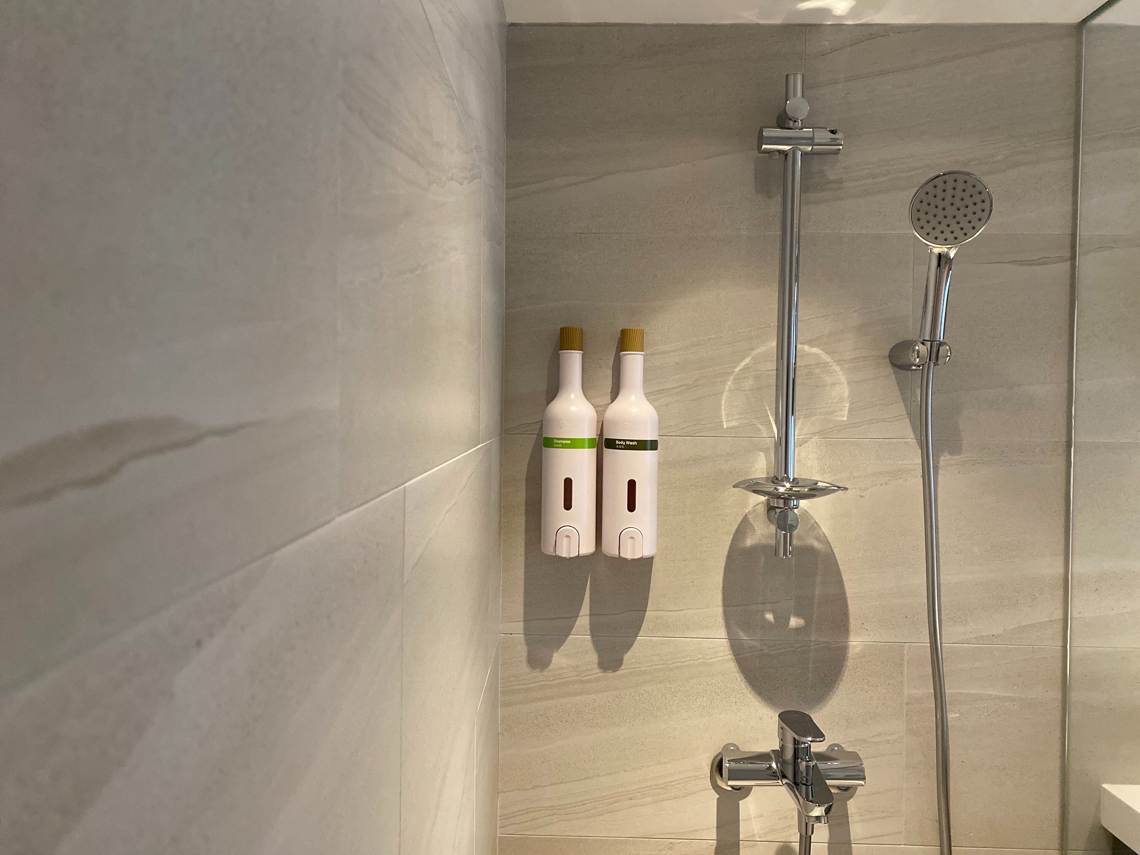 Une salle de bain avec une douche, deux flacons de gel douche et un porte-serviettes.