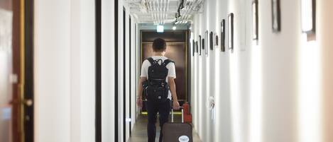 Corredor de hotel com uma pessoa caminhando em direção a uma porta, carregando uma mala.