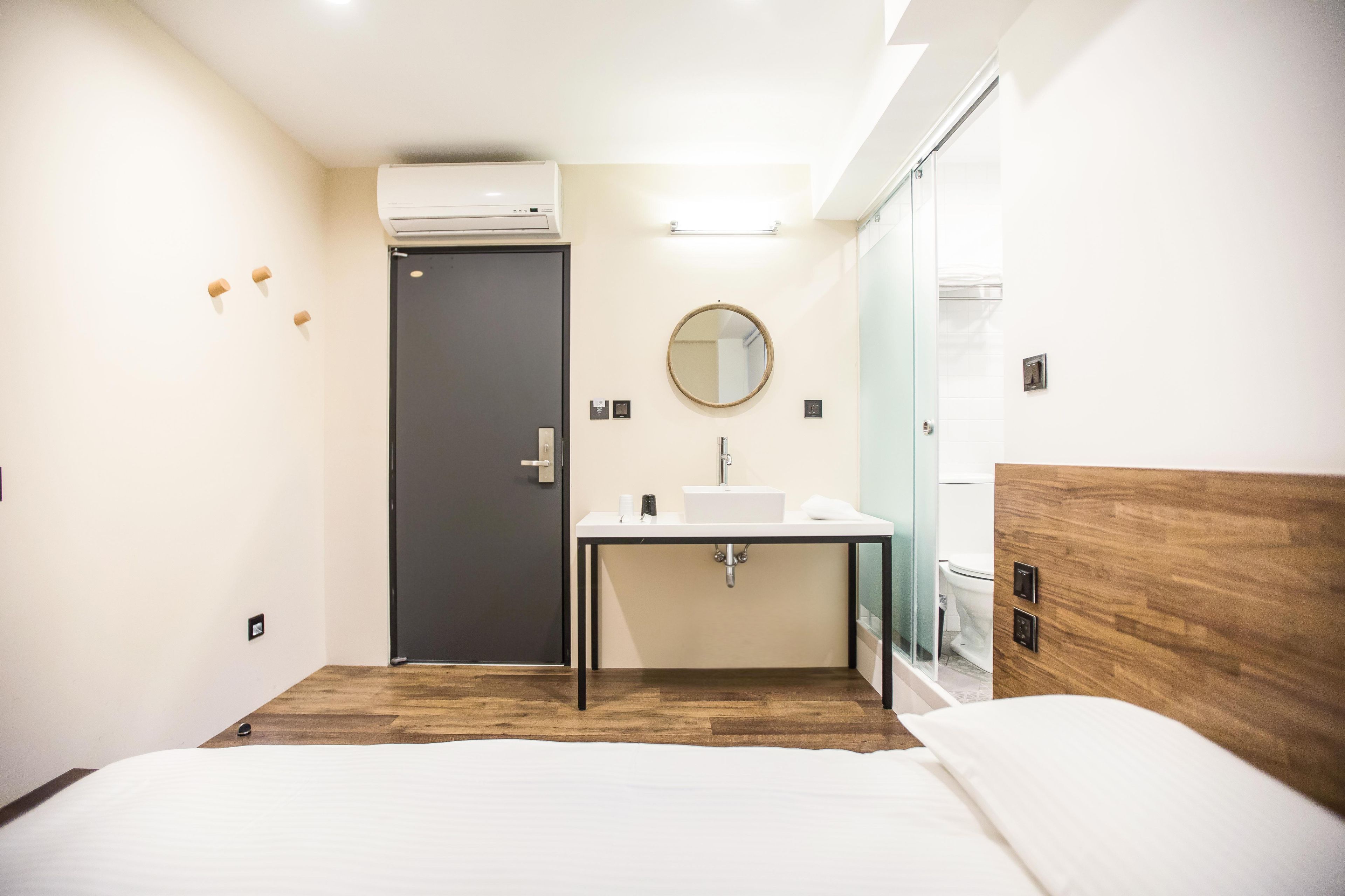 A modern hotel room with a bed, a bedside table, a sink, and a mirror.