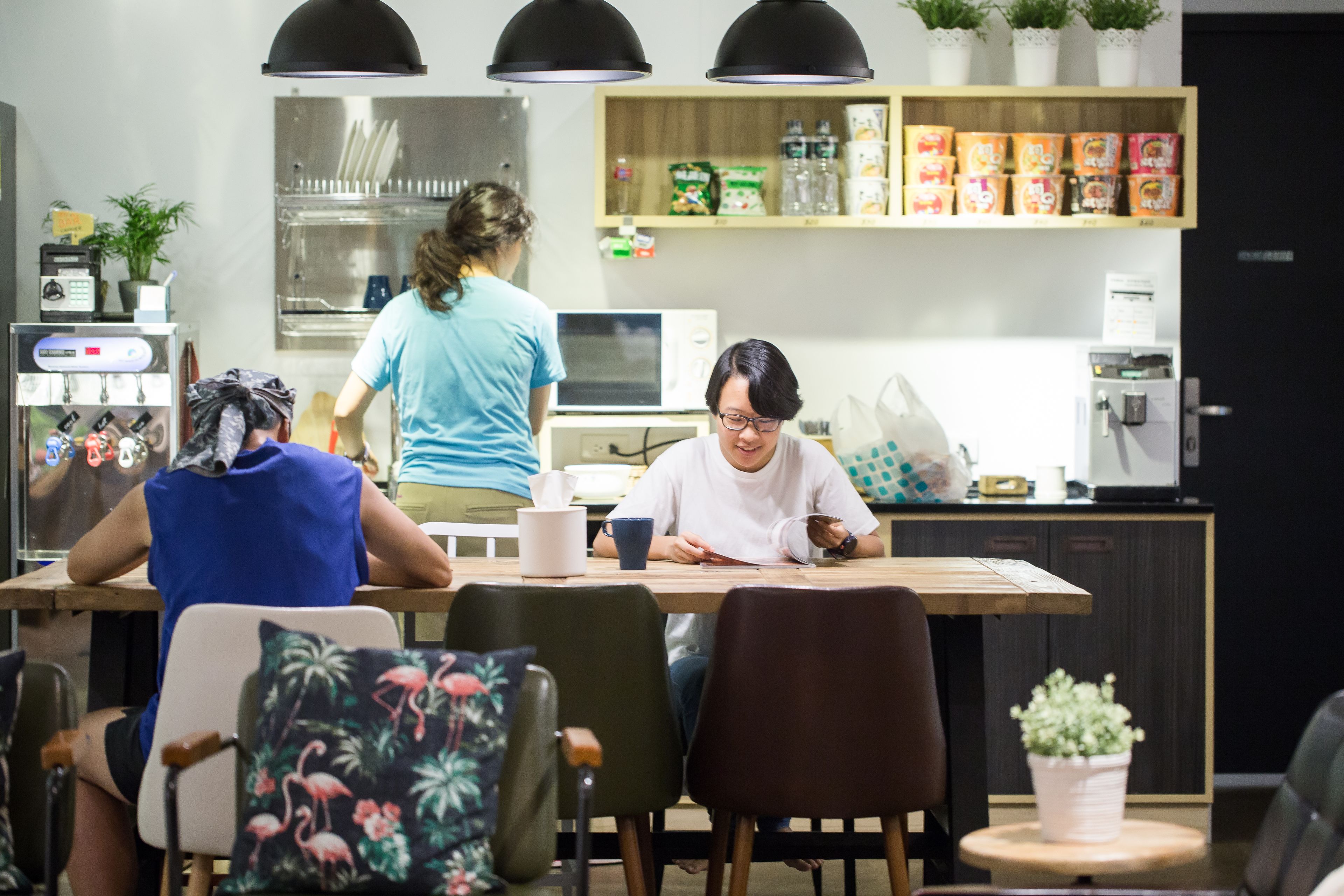 Una cocina moderna con una mesa de madera, sillas y un microondas. Hay plantas en macetas en los estantes y una cafetera en la encimera.