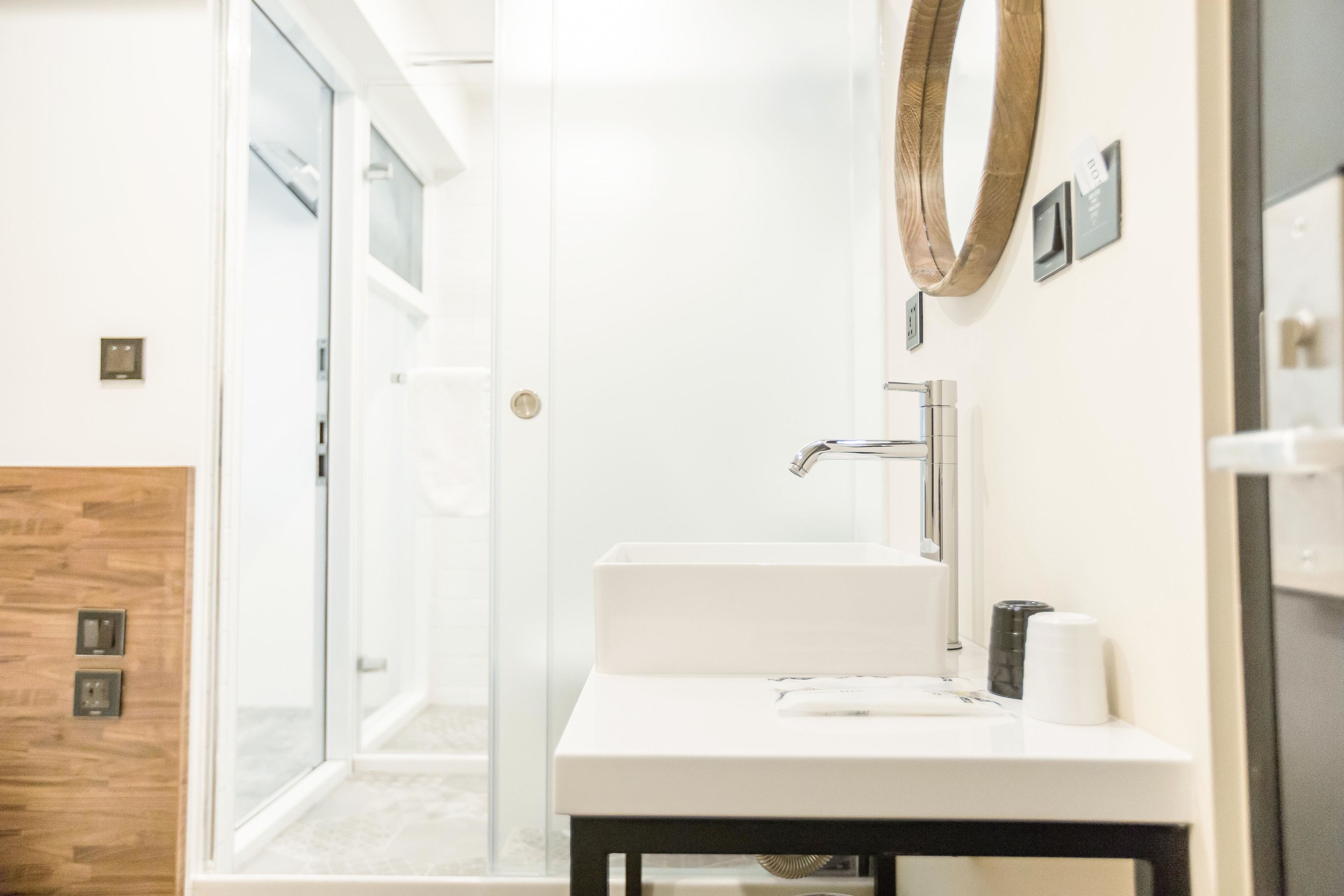 A modern bathroom with a glass shower door, a white sink, and a wooden accent wall.