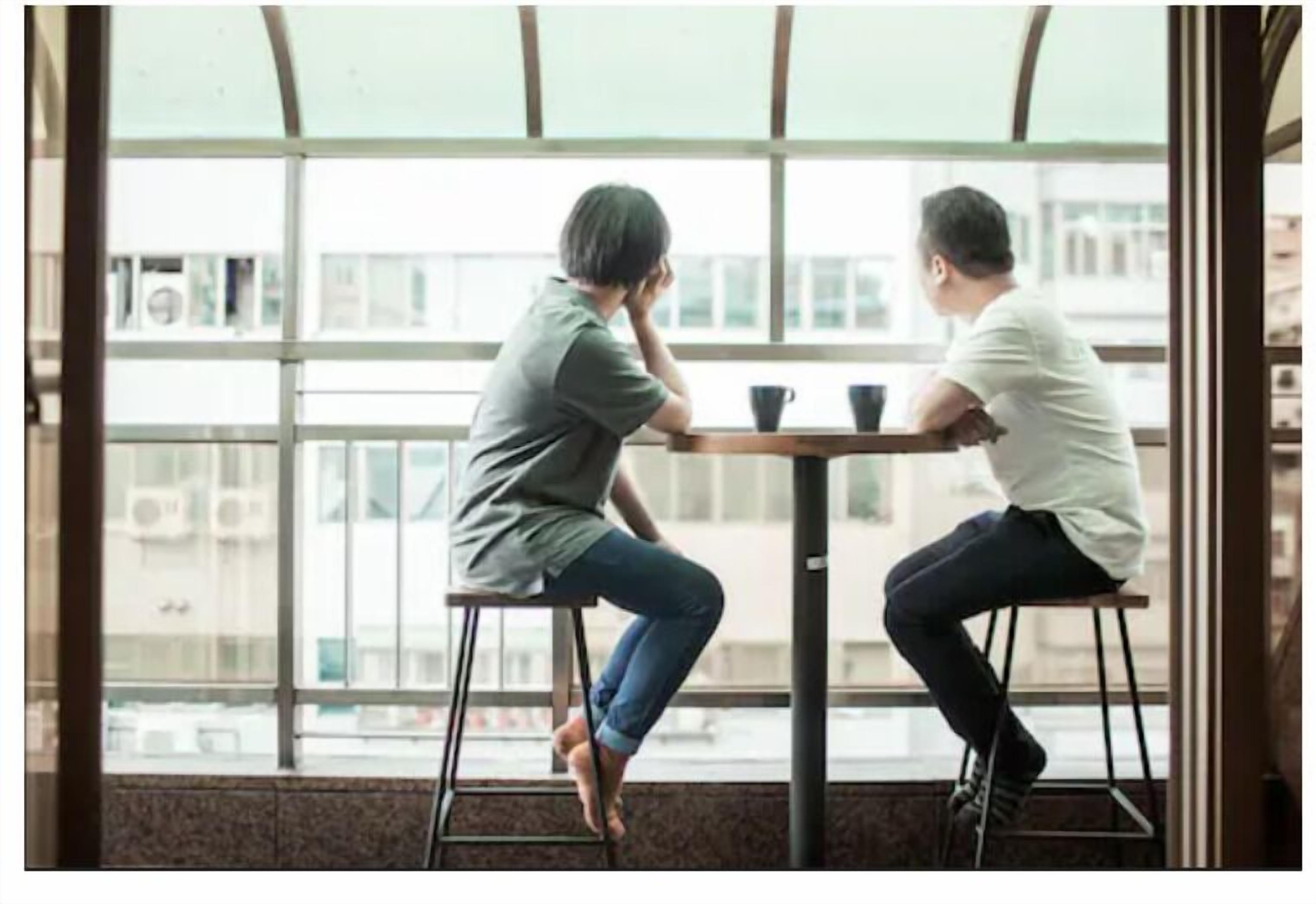 Two people sitting at a table in a room with large windows.