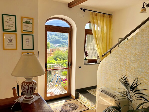 Una habitación con puerta de madera que da a un balcón, una mesa pequeña con lámpara y una escalera.