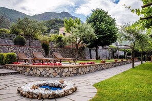 Un muro de piedra con un hogar, sillones de descanso y un jardín cuidado con plantas en macetas y una pequeña fuente.