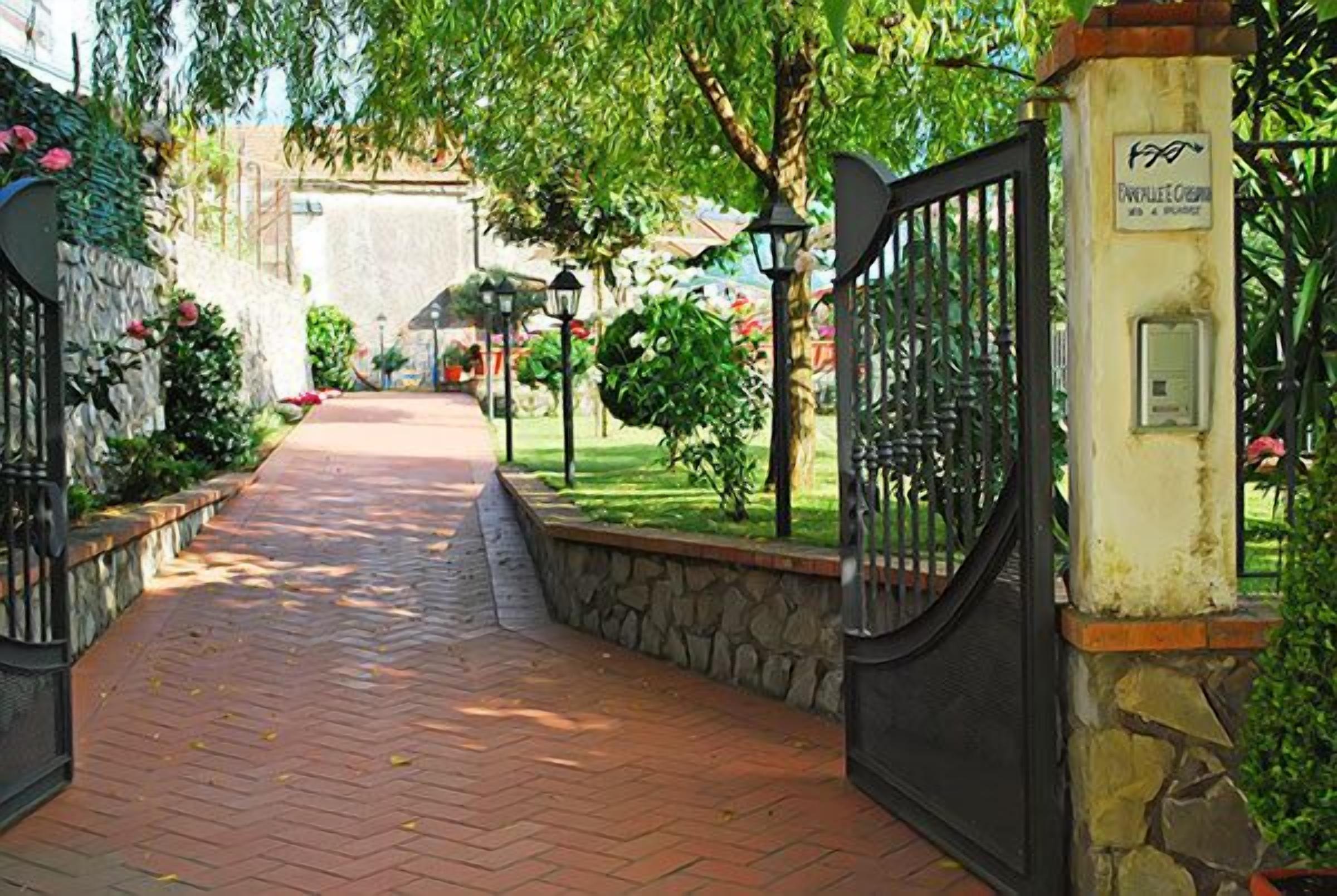 A paved pathway leading to a gated entrance with stone walls and greenery.