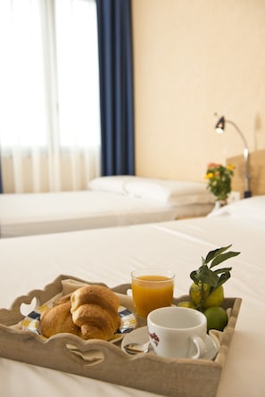 A breakfast tray with croissants, orange juice, and a cup on a bed in a hotel room.