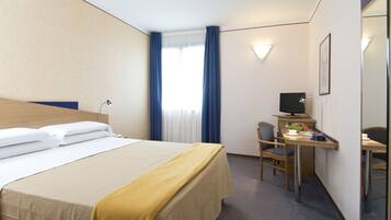 A hotel room with a bed, a desk, a chair, a television, and a window with curtains.