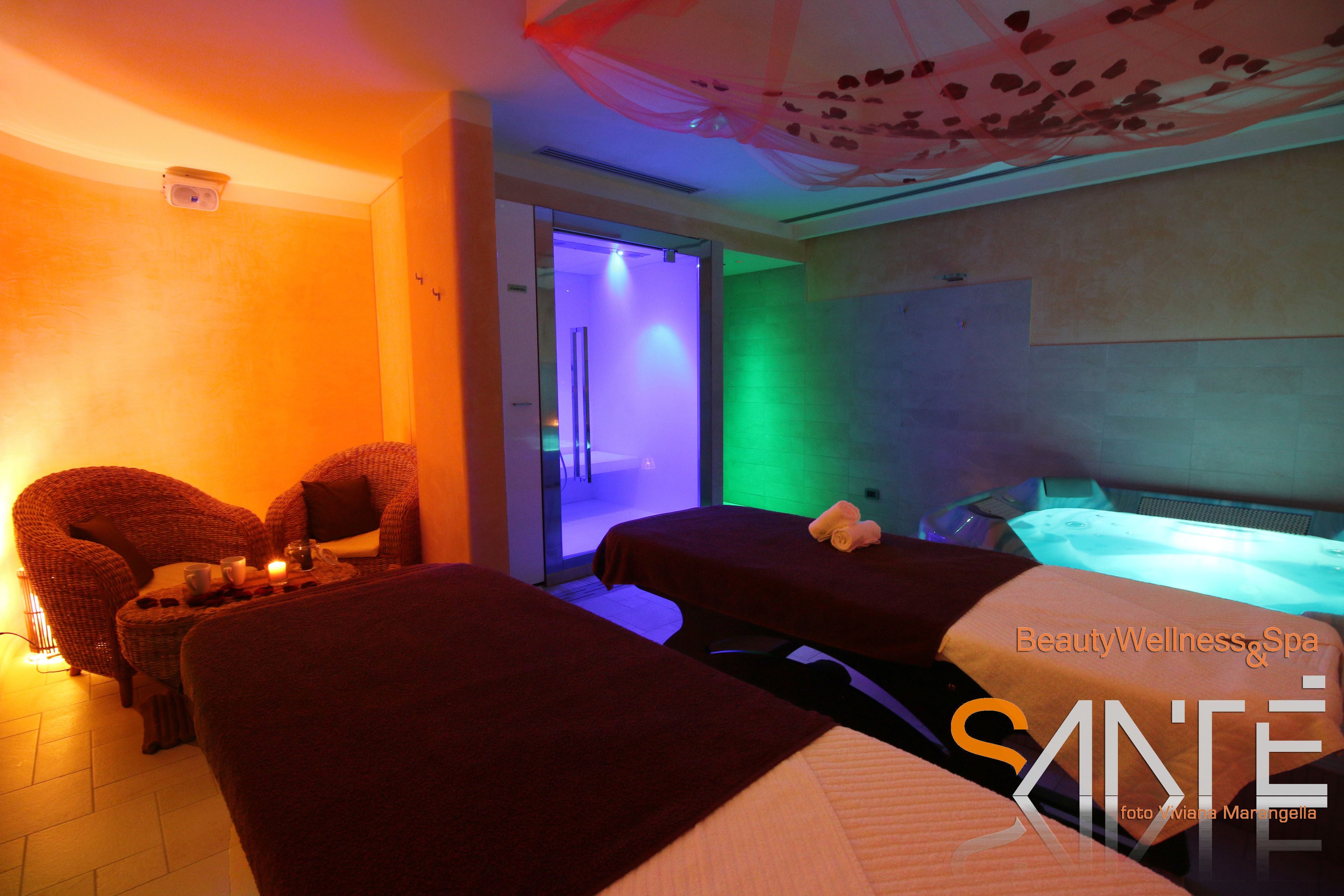 Een spa-ruimte met twee massagetafels, een stoel en een klein tafeltje met kaarsen.