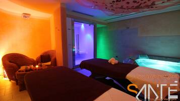 Een spa-ruimte met twee massagetafels, een stoel en een klein tafeltje met kaarsen.
