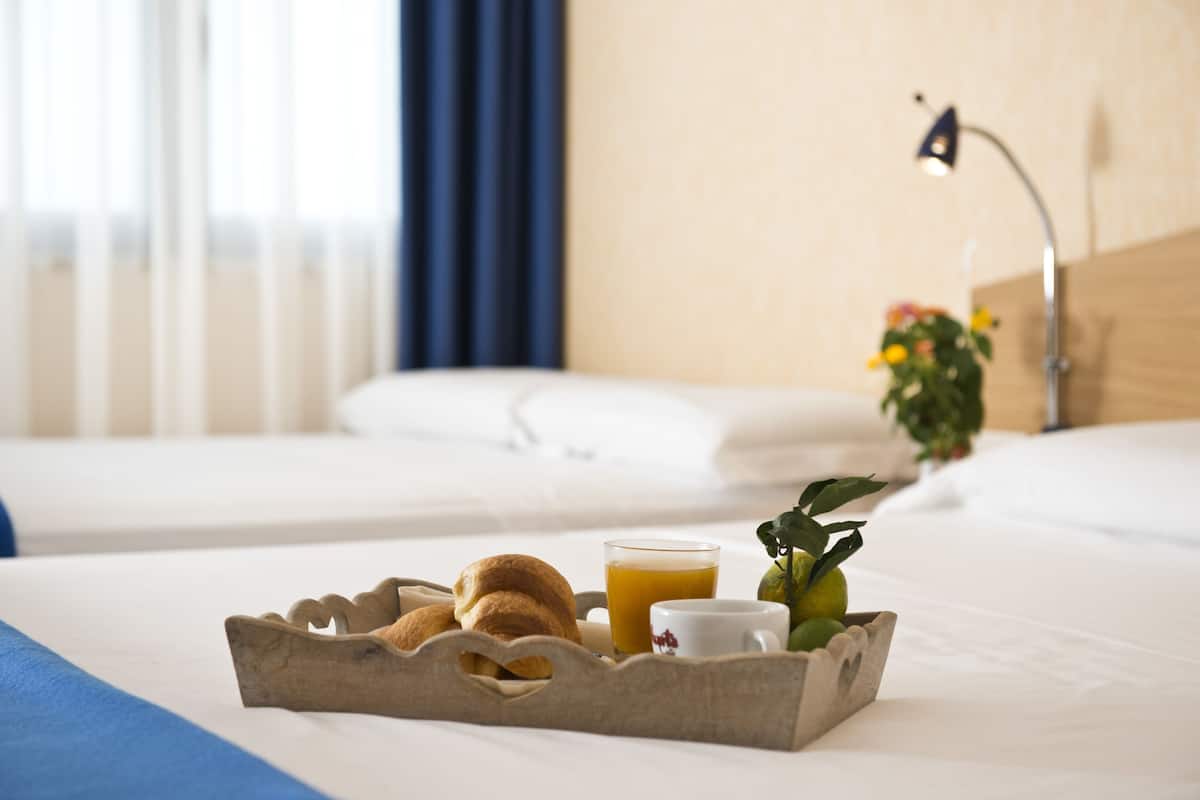 A neatly made bed with a tray of breakfast items including croissants, a cup of coffee, and a glass of orange juice.