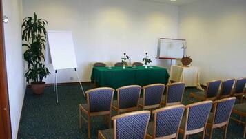 Une salle de conférence avec une table verte, des chaises, un tableau blanc et une plante en pot.