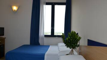 A hotel room with two beds, a TV, a window with curtains, and a plant.