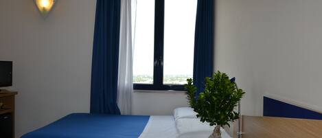 A hotel room with two beds, a TV, a window with curtains, and a plant.